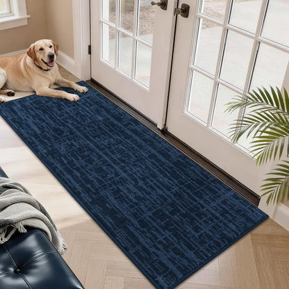Dog lying on a blue doormat in front of a glass door with a plant nearby.