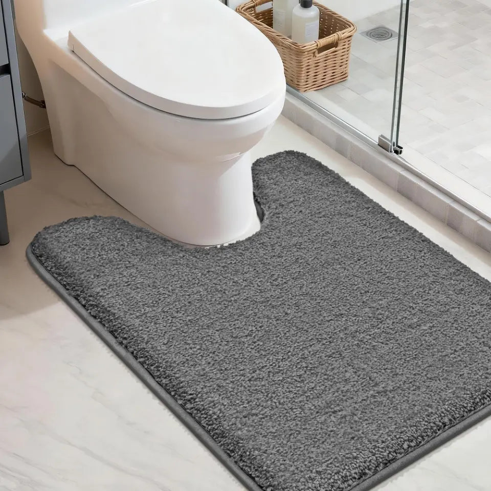Dark gray u rug in front of a toilet in a bathroom setting