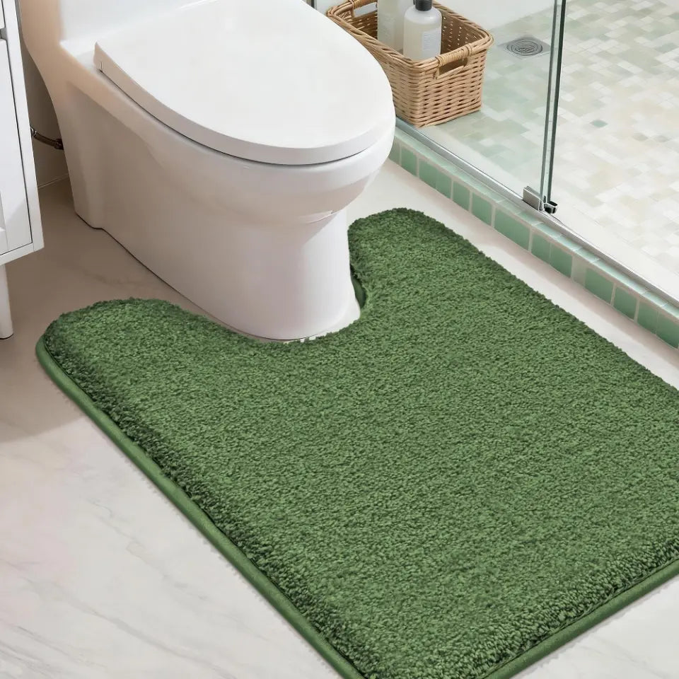 Green U shaped bath mat in front of a toilet in a bathroom setting